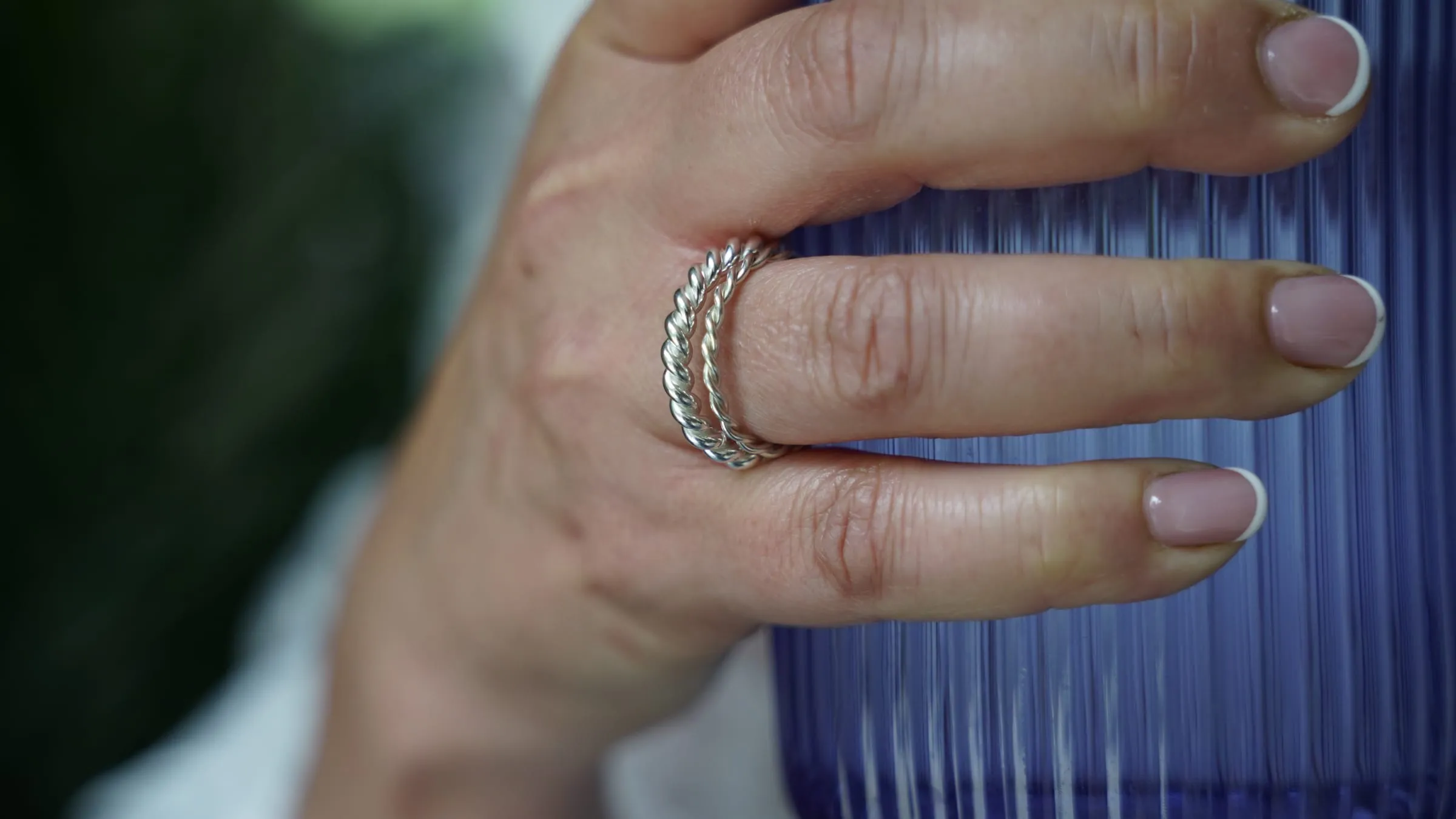 Stacked twisted silver rings on a finger, around a ribbed blue glass.