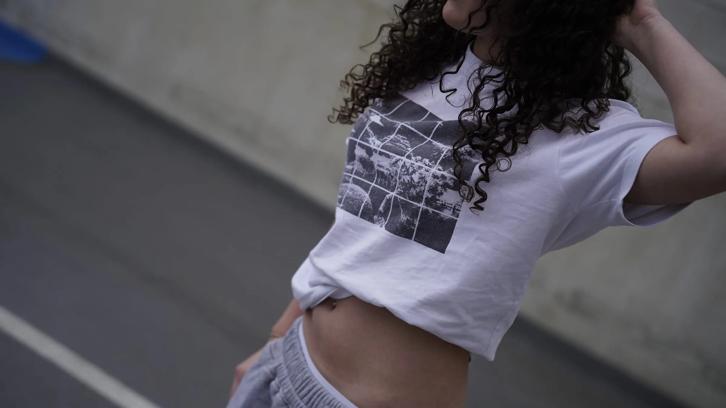 The print on a cropped white T-shirt, an arm raised against a concrete ramp.