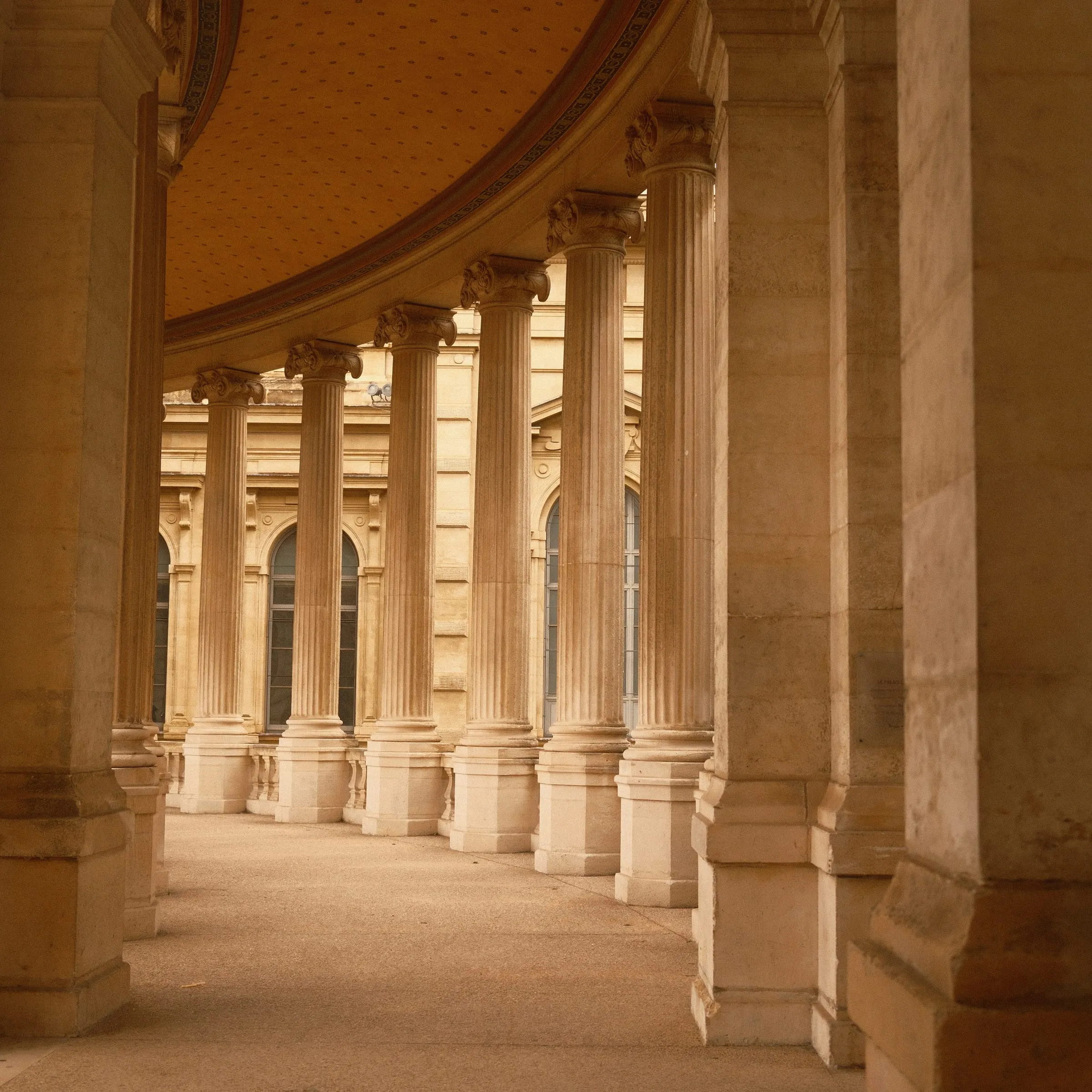 A curved colonnade of stone columns in warm, even light.