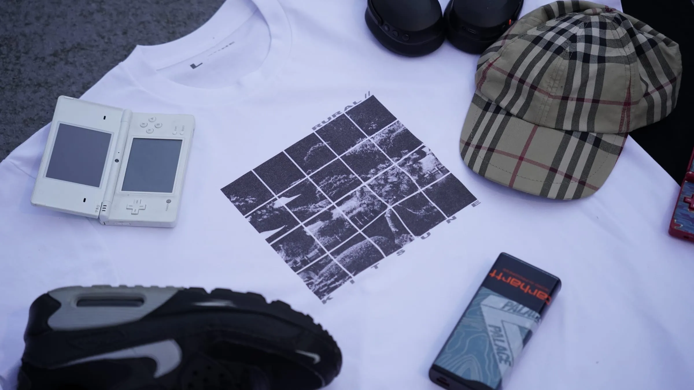 Flat lay: the T-shirt with trainers, a checked cap, a handheld console and a phone.