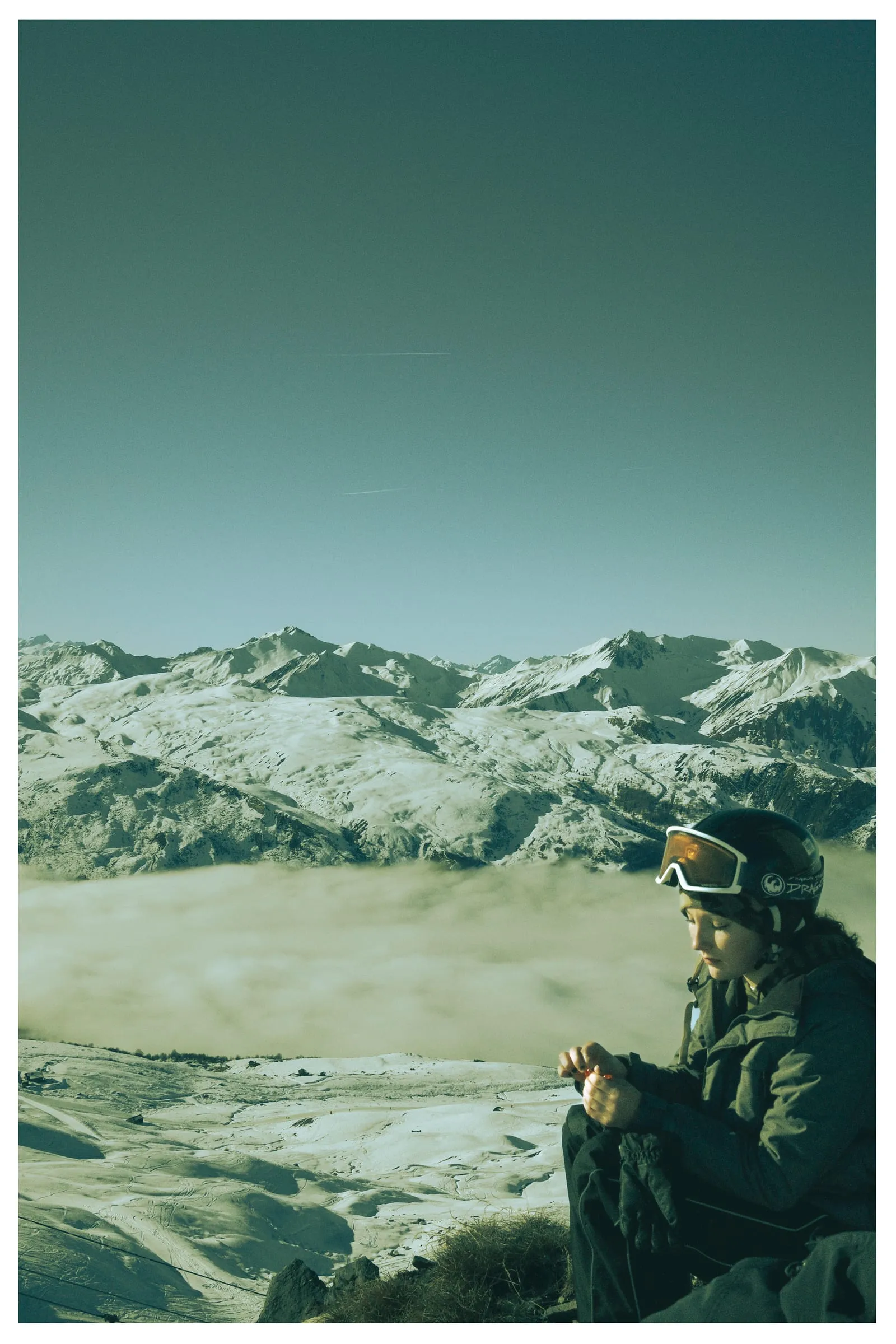 A skier sits in the snow above a sea of cloud, mountains behind.