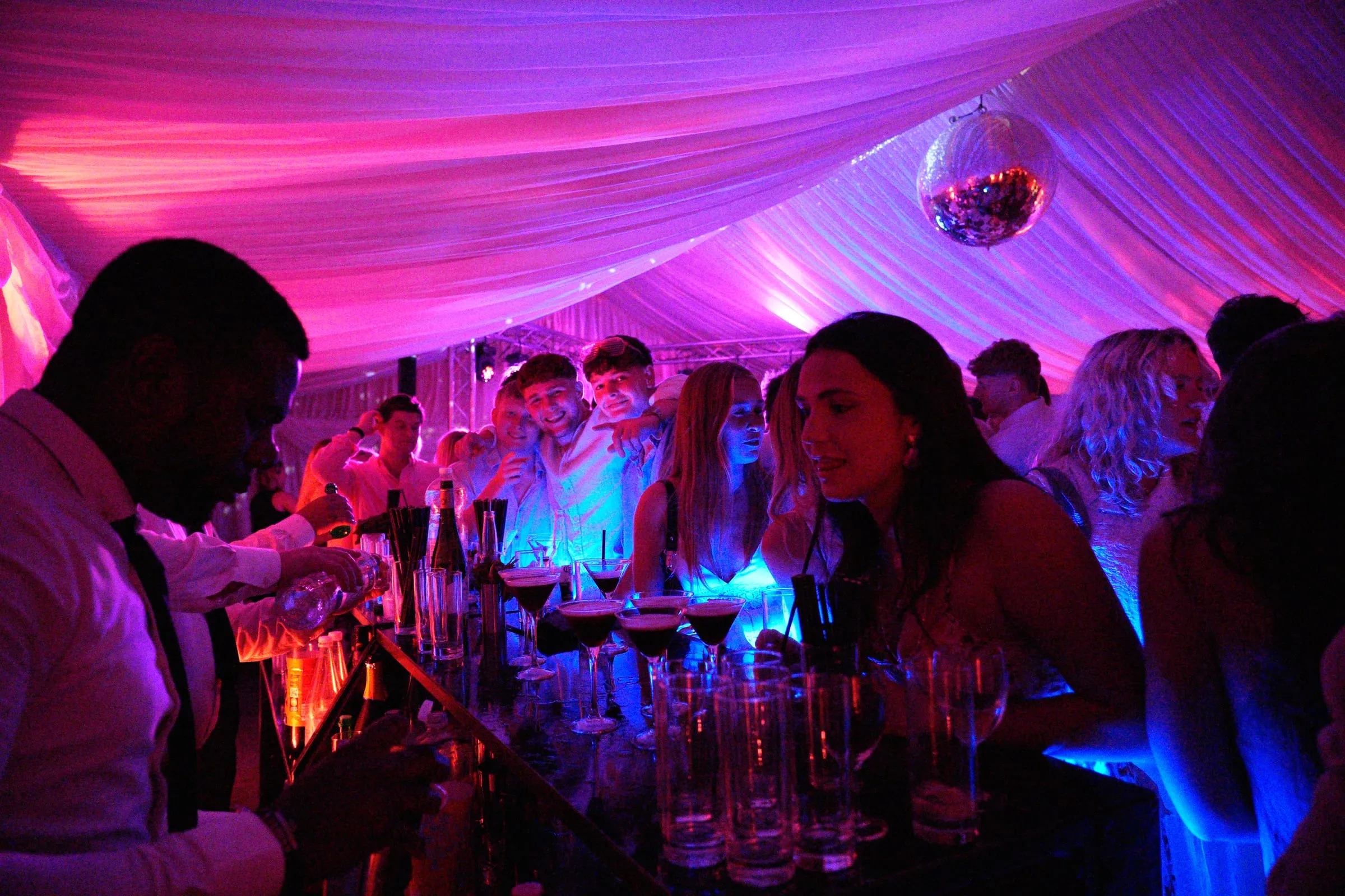 Guests crowded at the bar under pink light.